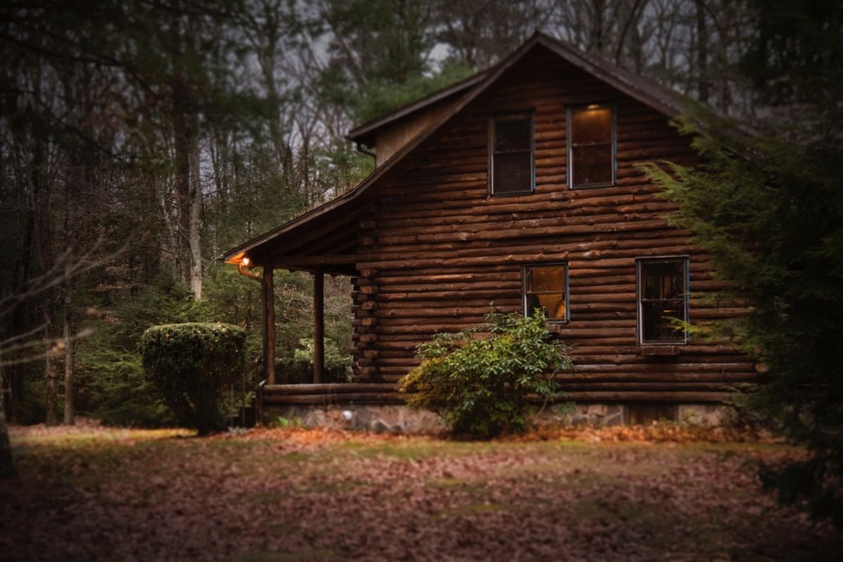 Edited photo of a two-storey log cabin at dusk with warm light glowing from the windows and porch.